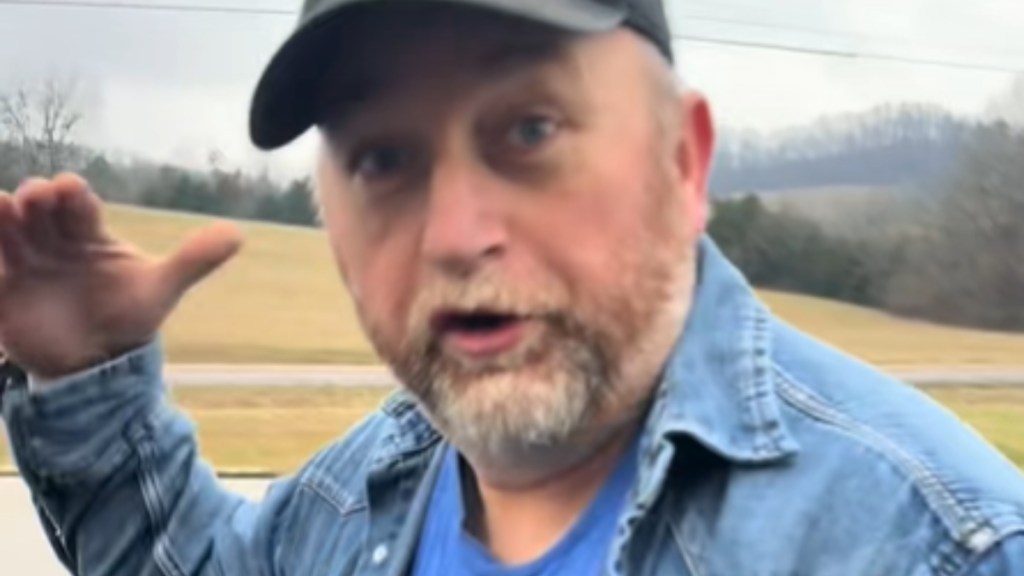 Close up of a man in a jean jacket and hat. He's standing outside. He looks at the camera as he talks, one hand raised as he demonstrates something