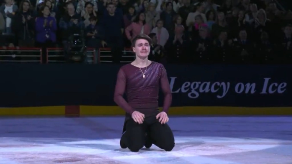 Ice skater Maxim Naumov rests on his knees on the ice. He cries as he looks into the crowd